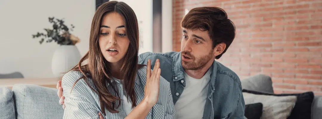Image of an unhappy woman sitting with her hand in a stop motion next to a man talking to her
