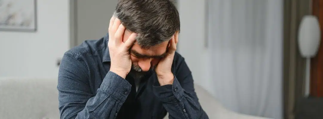 Image of a man in anguish sitting down and looking at the ground with his hands on his forehead