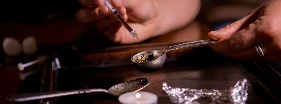 Image of a syringe and needle beside a spoon of black tar heroin 