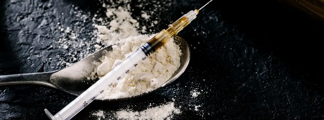 Image of a syringe on top of spoon overloaded with white powder heroin