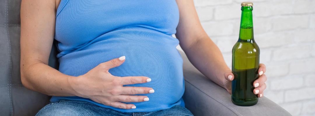 Image of a pregnant woman holding a bottle of non-alcoholic beer, highlighting the risks of any alcohol consumption during pregnancy