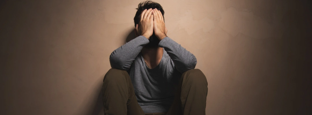 Image of man sitting on the floor against a wall with his hands on his face, struggling with addiction losing control over daily life and decision-making