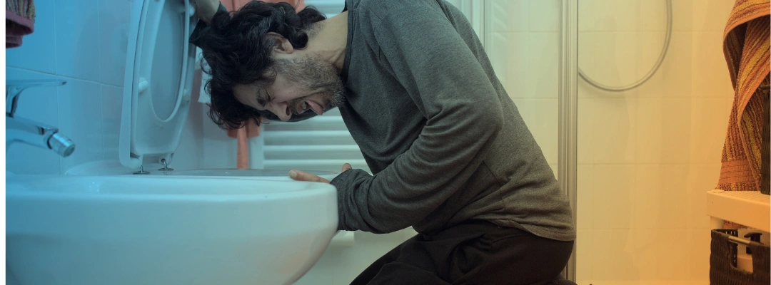 Image of a man kneeling in front of a toilet displaying symptoms of an overdose