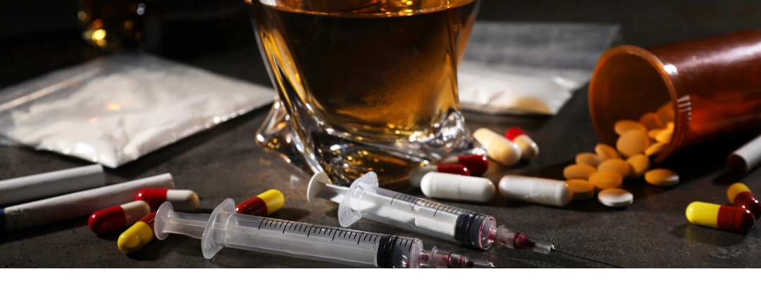 Image of various drugs in pill and syringe form, alongside a glass of whiskey, representing the risks of laced substances