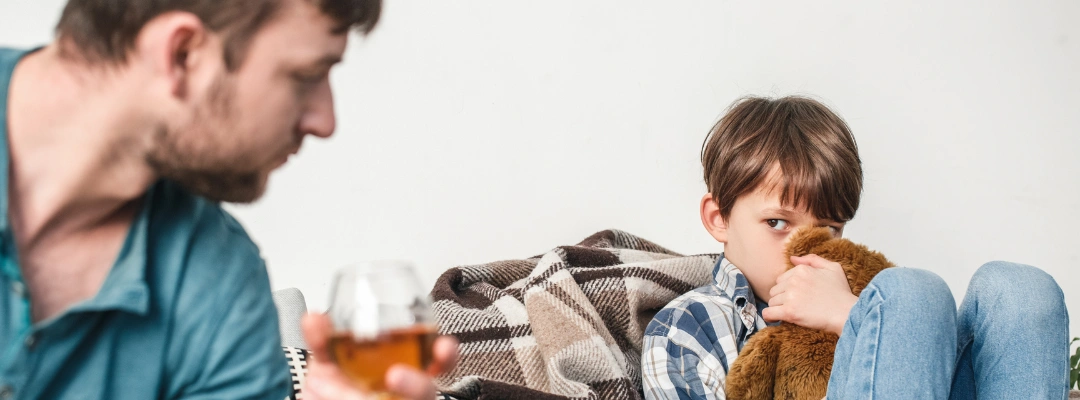 Image of young boy trying to protect himself with a tedd bear as his distraught father looks on - Alcoholism Genetic - Purpose Healing Center